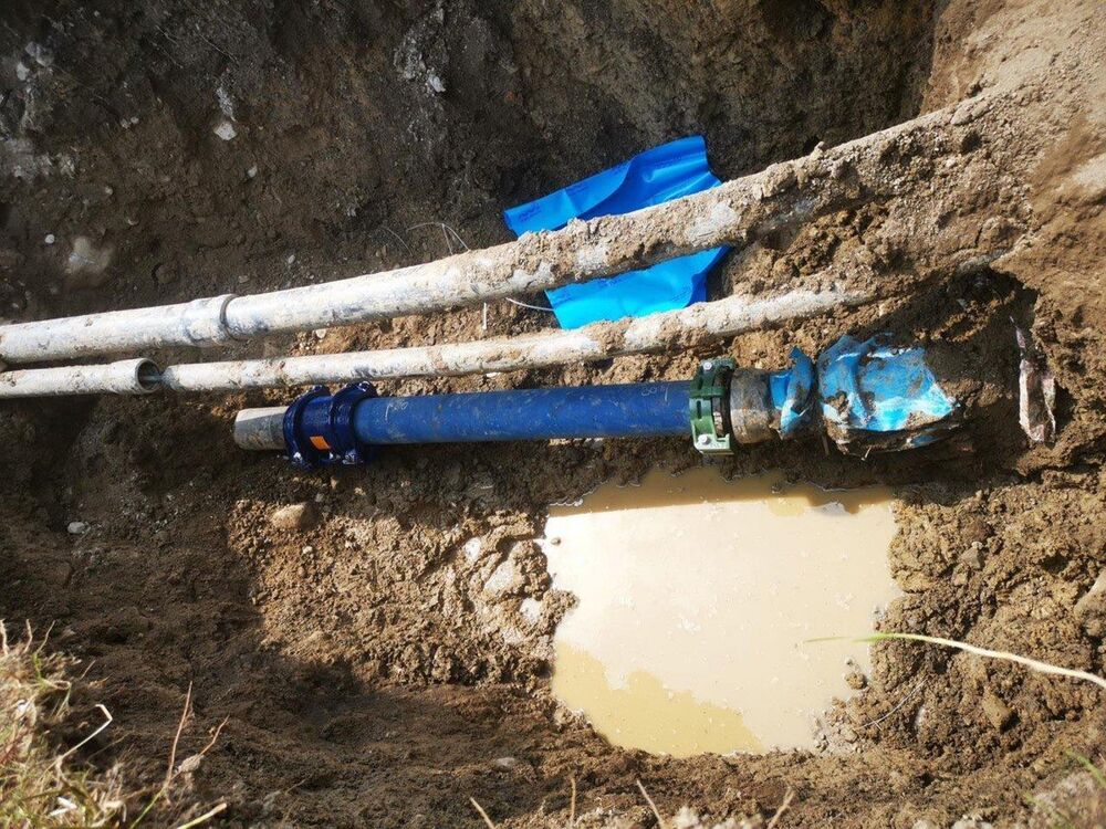 Leitungsreparatur an einer Wasserleitung (blaues Rohr). Im Bild links ist das auseinandergezogene Kabelschutzrohr einer Elektroleitung zu sehen. Das Kabel darin ist intakt geblieben.